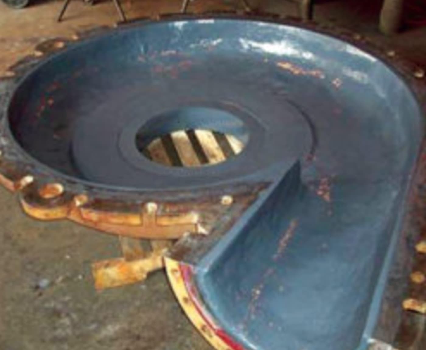 Split pump casing on a shop floor showing the volute passage and cutwater coated dark blue-gray