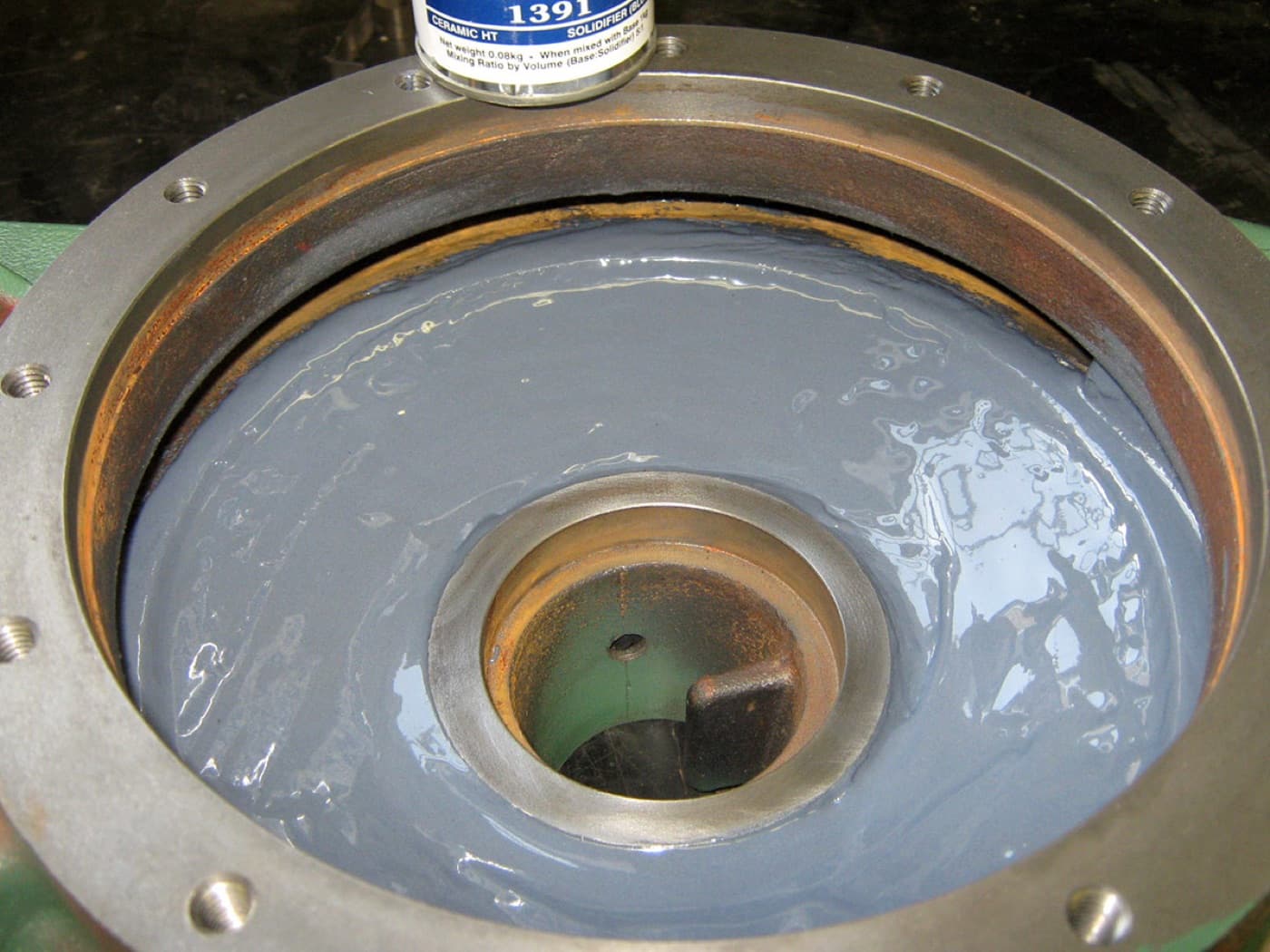 Machined circular housing with a bolted flange face, its internal bore coated with a smooth gray compound; a solidifier tin stands on the rim