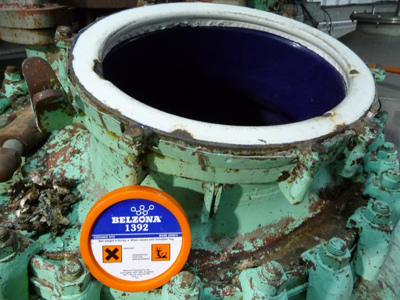 Green painted vessel with an open manway showing a deep blue ceramic-filled internal lining; an orange product lid rests on the casing