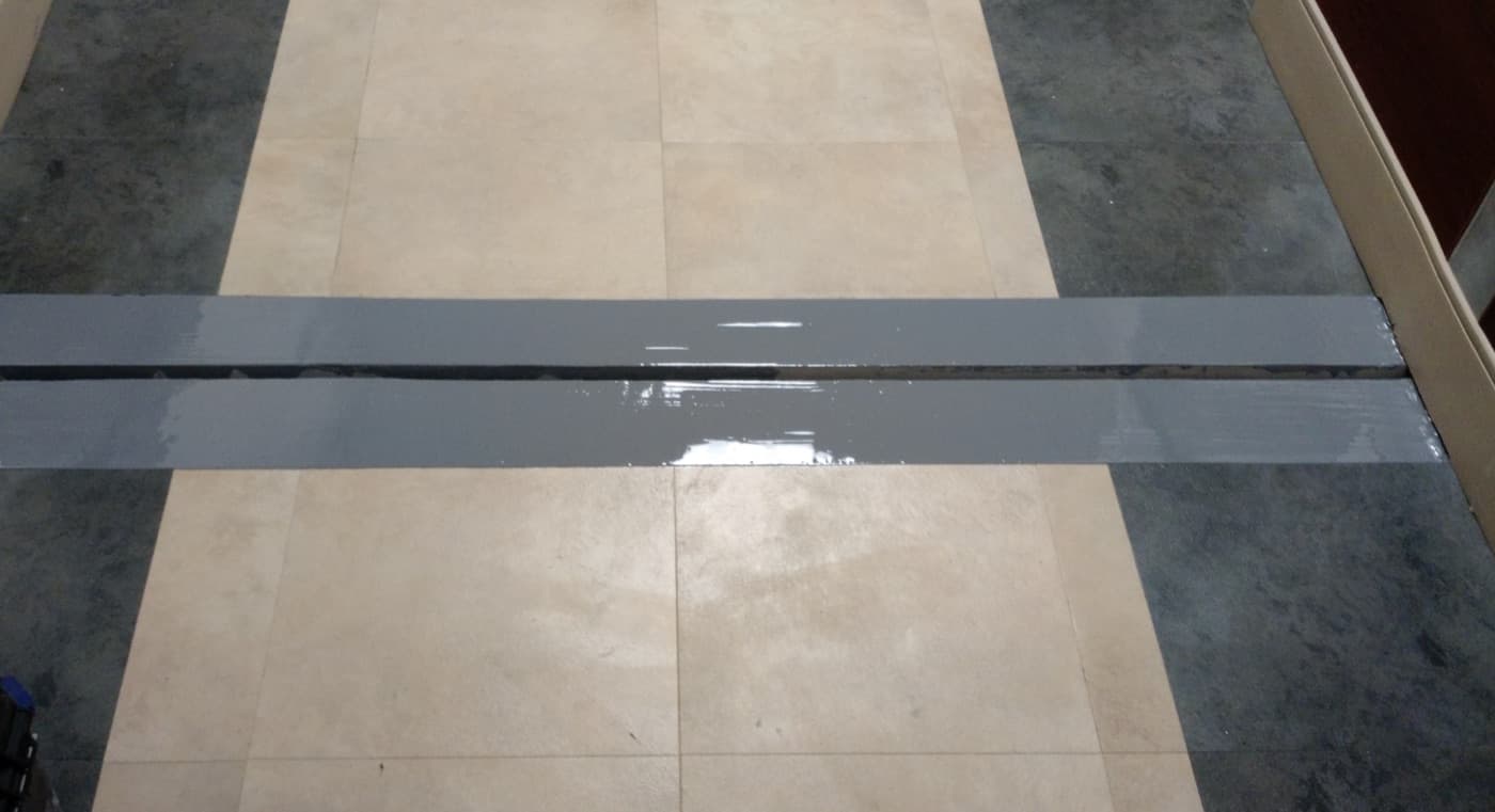 Gray flexible joint band running across a tiled floor between two paving bays