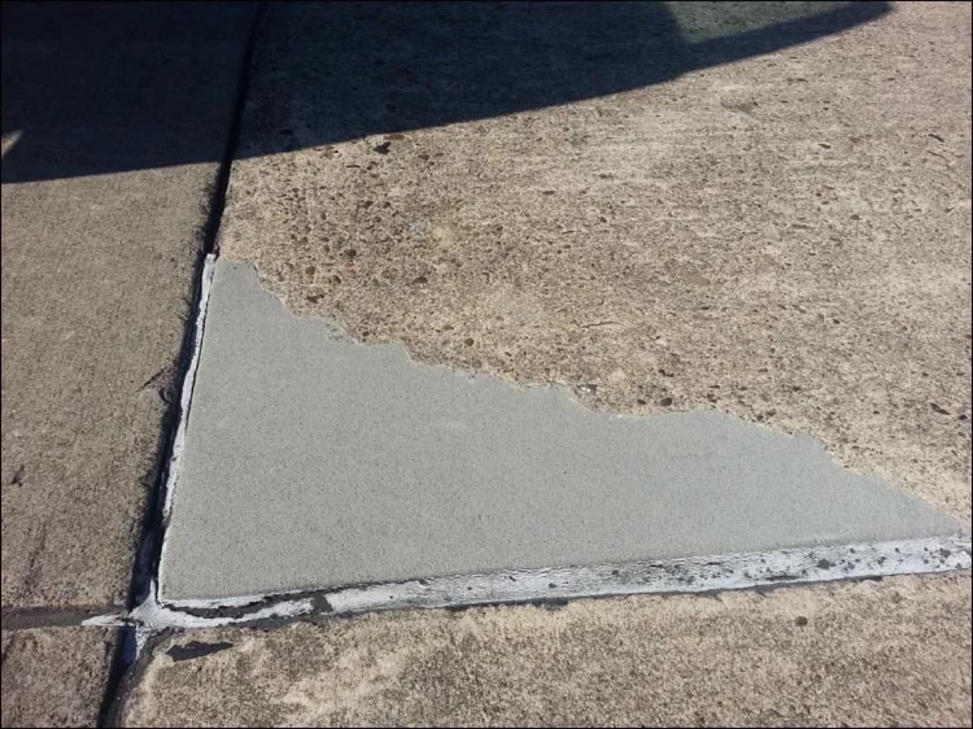 Outdoor concrete slab corner with a pale gray resurfacing patch feathered over spalled and exposed aggregate