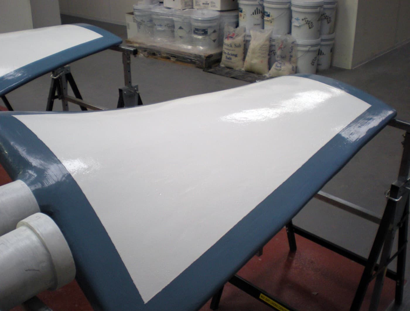 Two large blue fan blades on trestles in a warehouse, each with a white protective coating applied to its working face