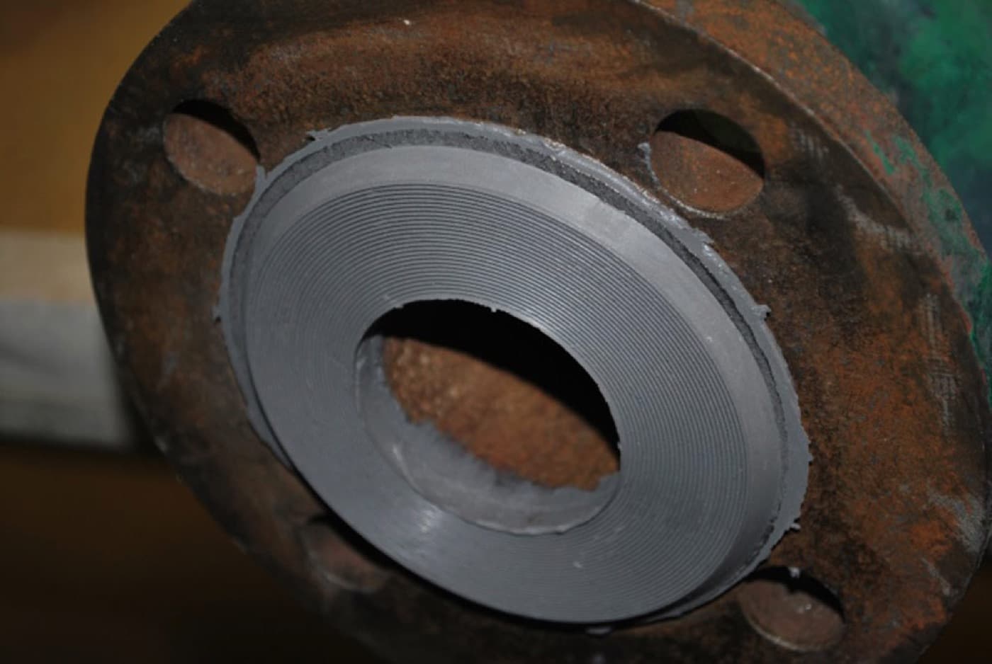 Corroded pipe flange whose raised face has been rebuilt in dark gray compound and machined with concentric serrations