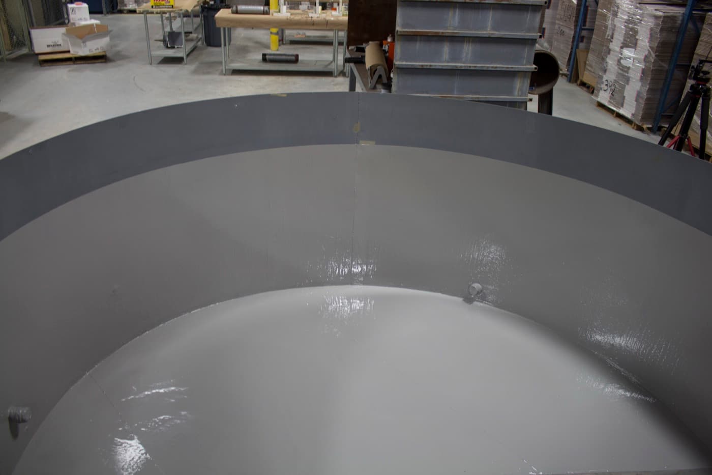 Dished vessel head standing on a shop floor, its interior coated in two tones of gray, still wet