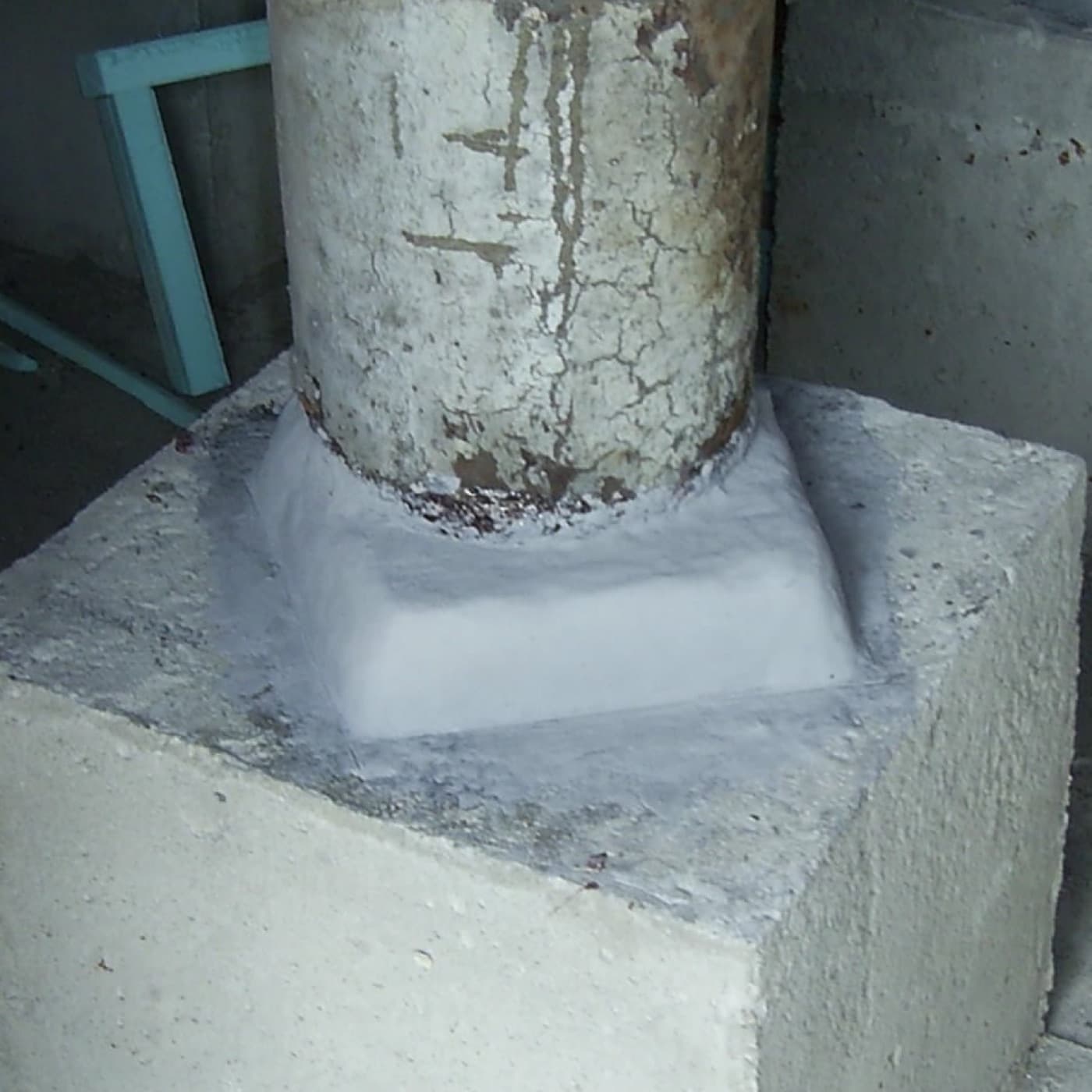 Spalled concrete column base on a plinth with a pale epoxy haunch cast around the foot of the column