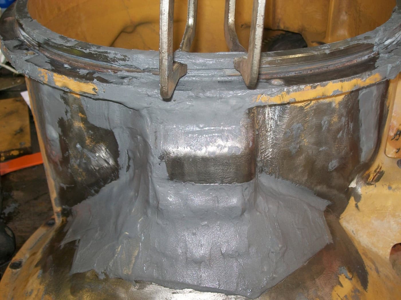 Yellow cast pump casing with gray repair compound trowelled over the flange face and body to rebuild lost metal