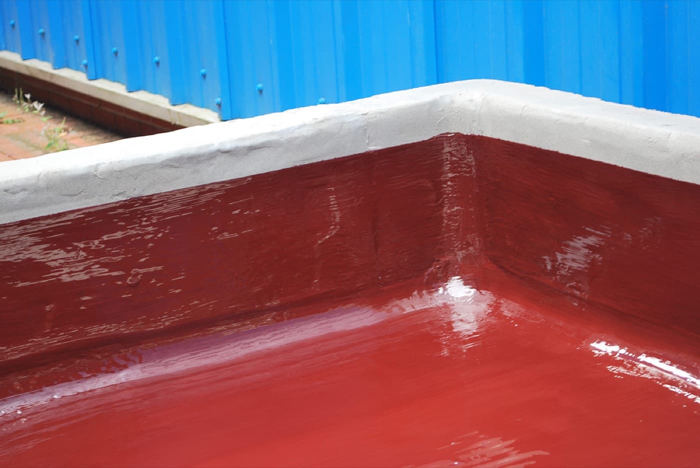Outdoor concrete containment bay lined with a glossy dark red chemical-resistant coating and finished with a white capping