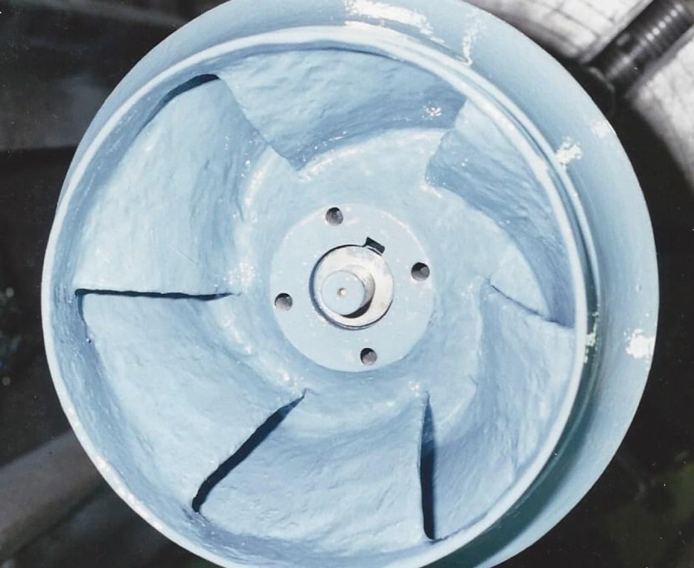 Open-faced pump impeller viewed head-on, its vanes and shroud coated pale blue