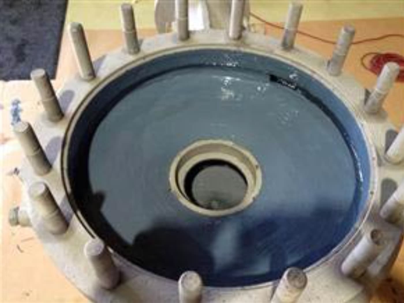 Large studded flange cover with its inner face coated in a glossy dark blue-gray finish