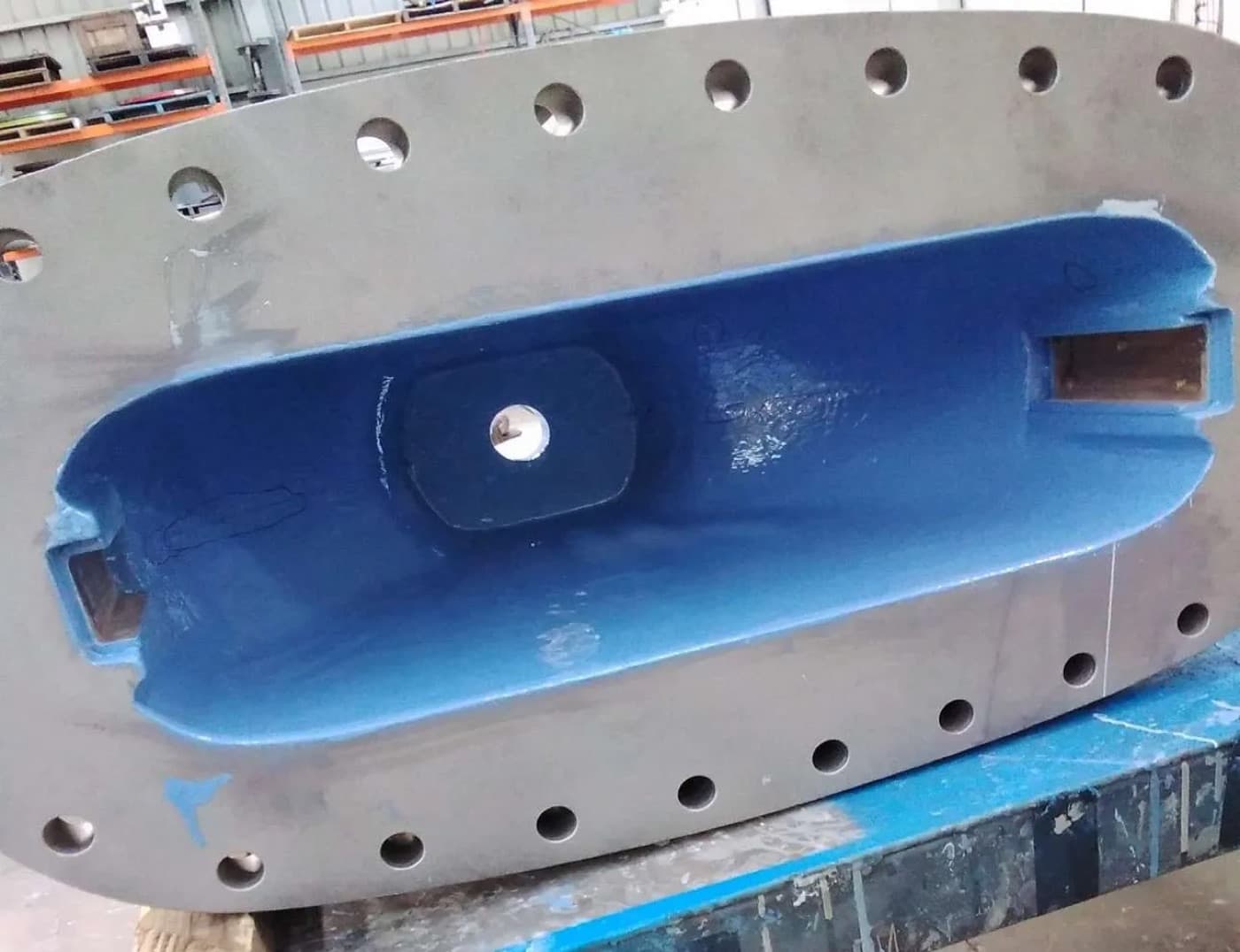 Oval flanged cover plate on a workshop bench, its machined recess coated bright blue
