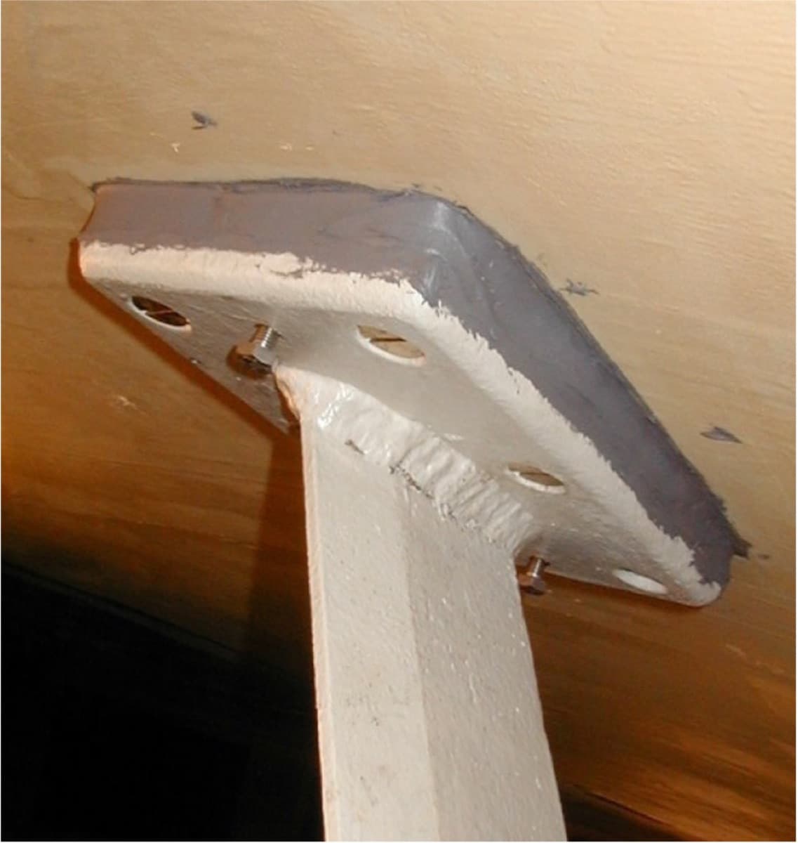 Handrail stanchion base plate bonded to the underside of a deck with gray adhesive squeezed out around its edge