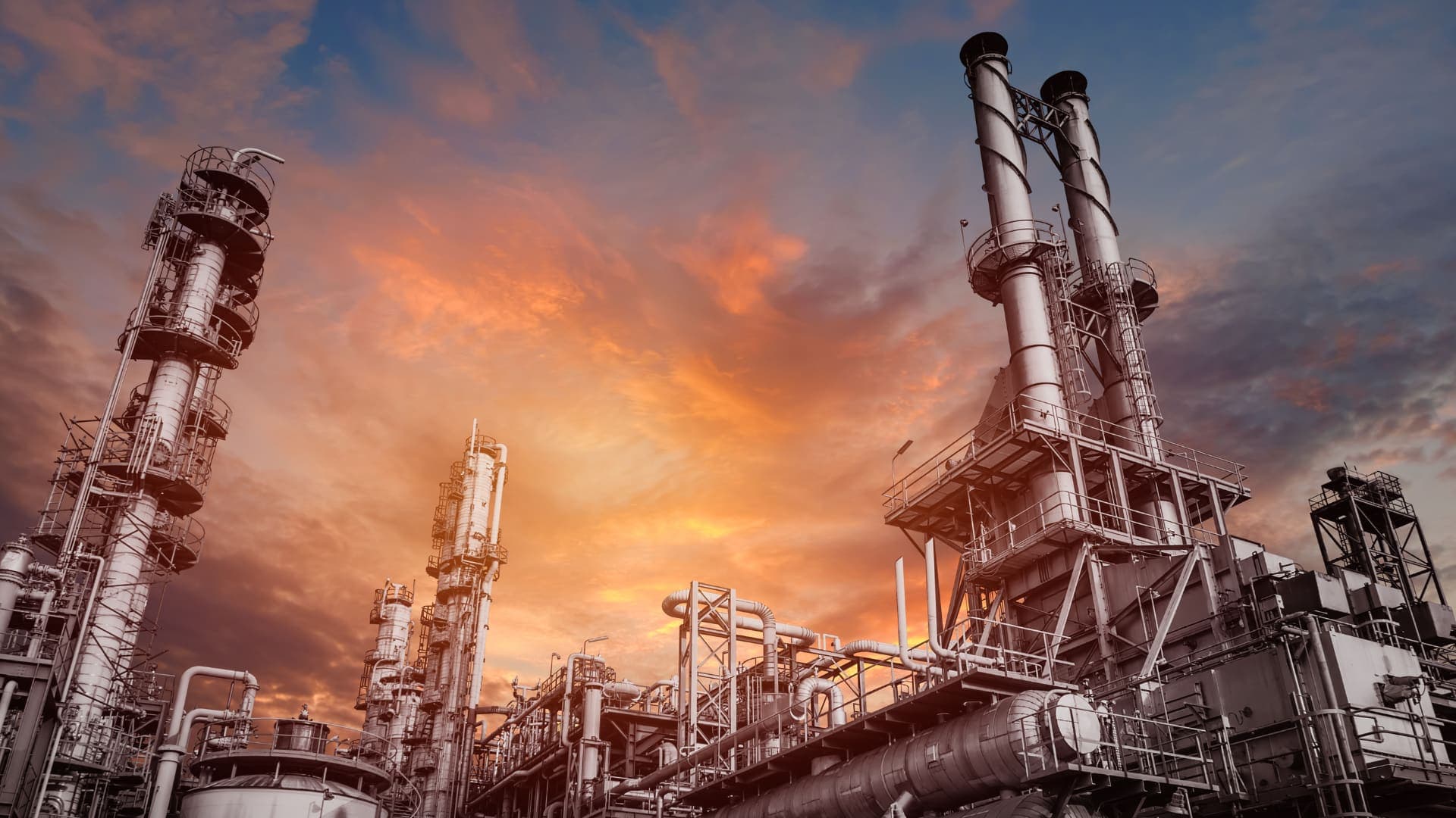 Refinery fractionation columns, stacks and pipe racks silhouetted against an orange and blue sunset sky