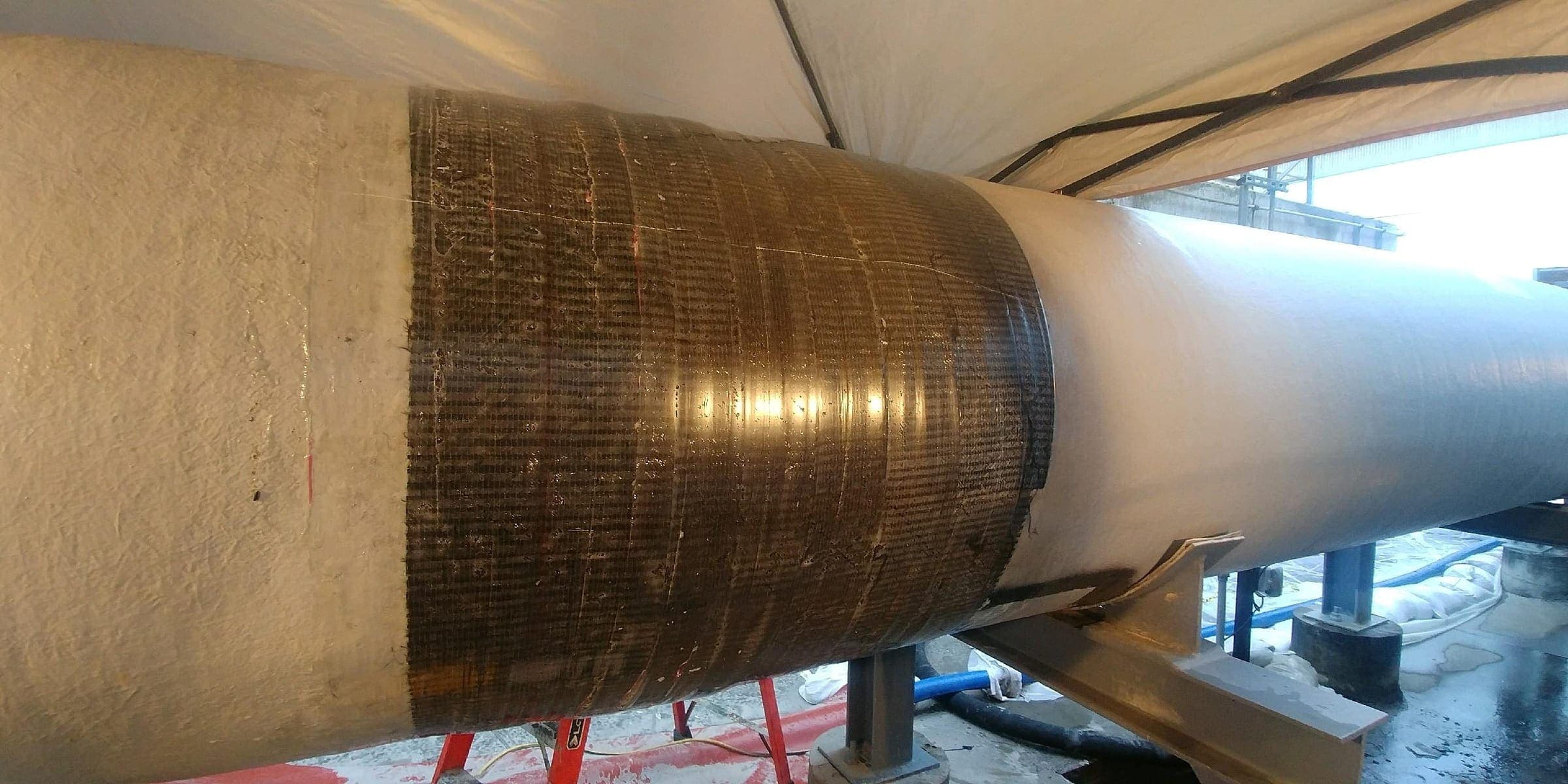 Large diameter insulated pipe inside a containment tent, with a cured composite wrap band applied right around the repair